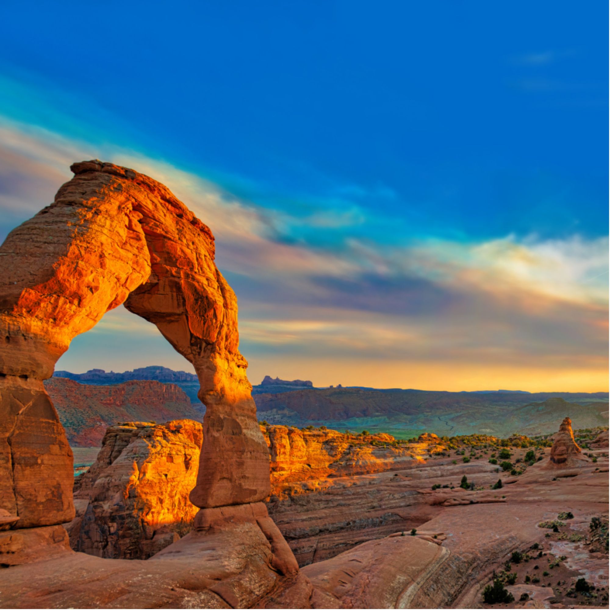 A natural sandstone arch standing strong above a rugged desert landscape at sunset, symbolizing the resilience, endurance, and strength rural communities need to overcome challenges and build a sustainable future.