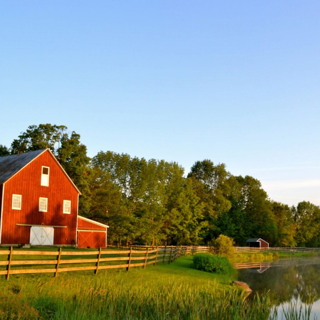 A red barn overlooking a quiet pond and open pasture, representing the rural communities at the heart of healthcare and the importance of preserving strong local resources for future generations.