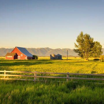 Agricultural landscape featuring a red barn, fields, and distant mountain range.