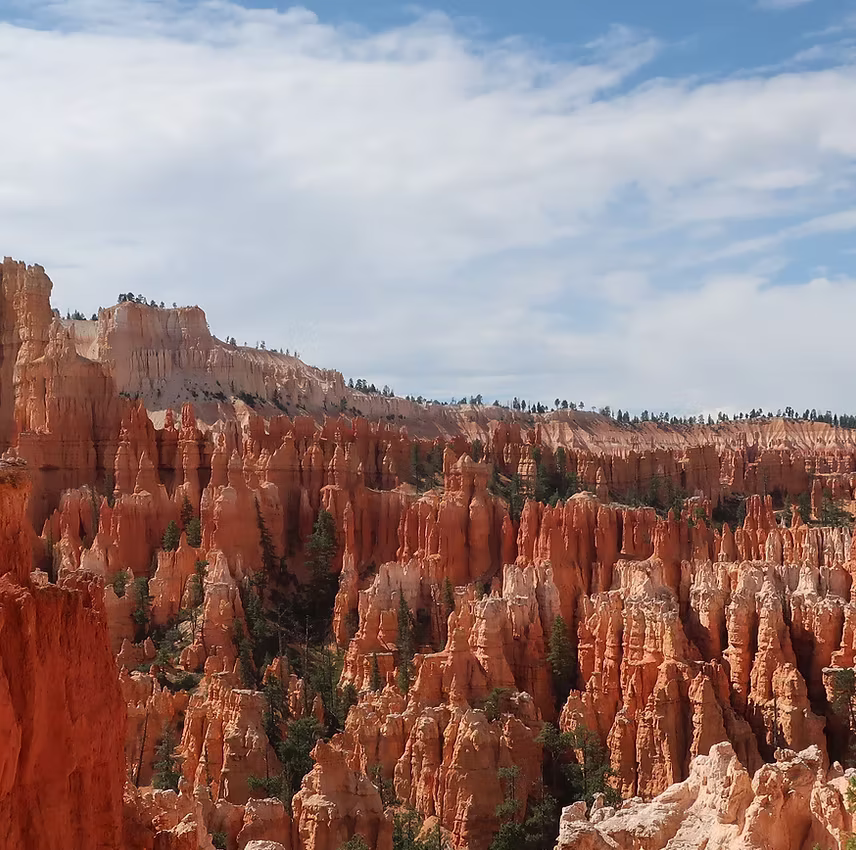 View of Bryce Canyon's red rock hoodoos under a partly cloudy Utah sky.