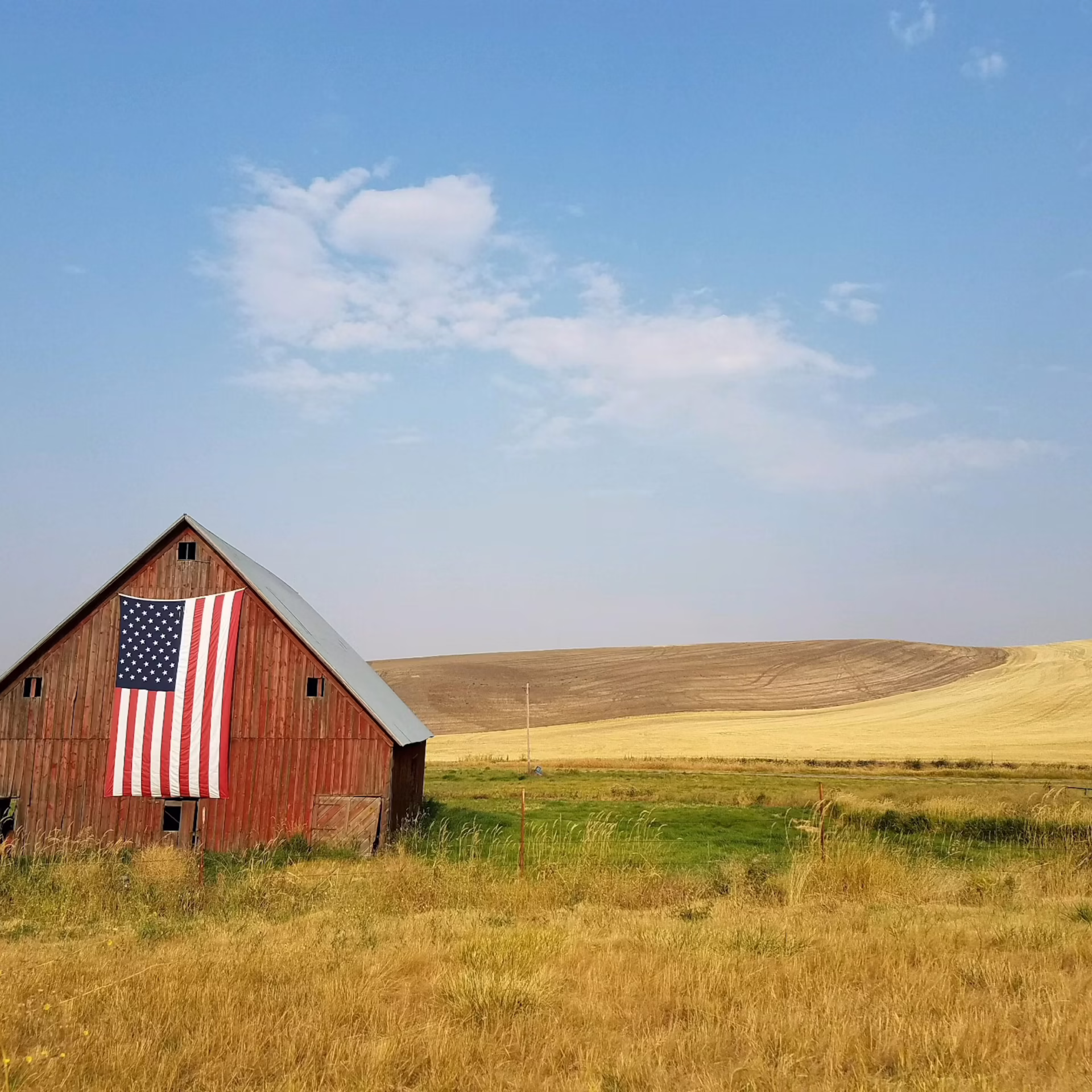 Red barn displaying an American flag beside rolling farmland and open fields.