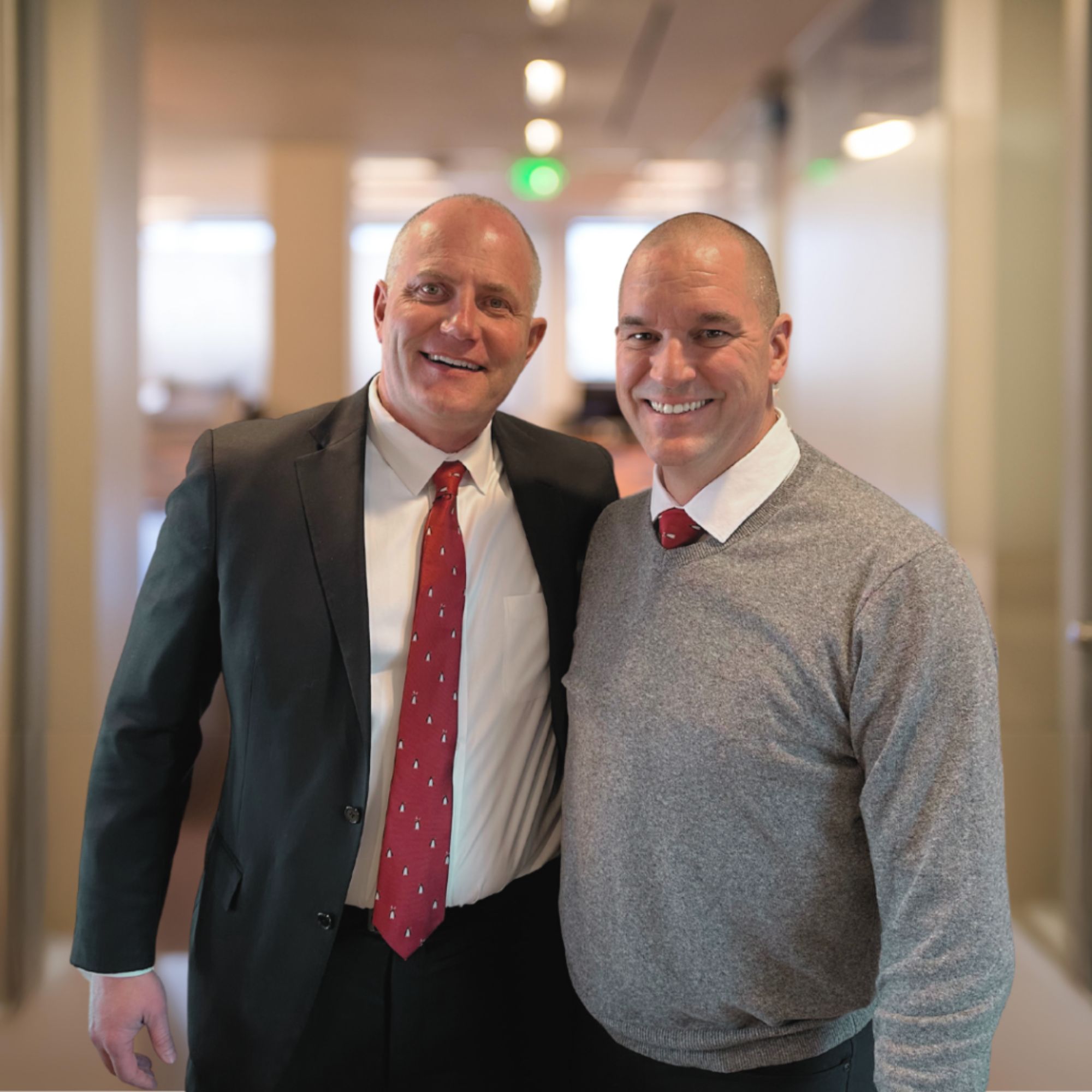 Jeff and John stand together in a bright office hallway, smiling at the camera and representing the leadership, partnership, and people-first approach that drive meaningful impact.