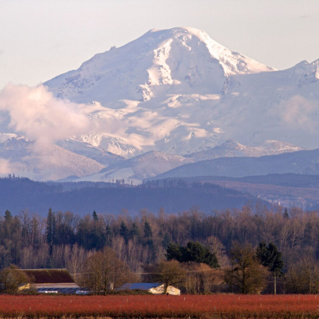 Rural farmland set against a snow-covered mountain backdrop, reflecting the remote and underserved communities that rely on strong local healthcare access and support.