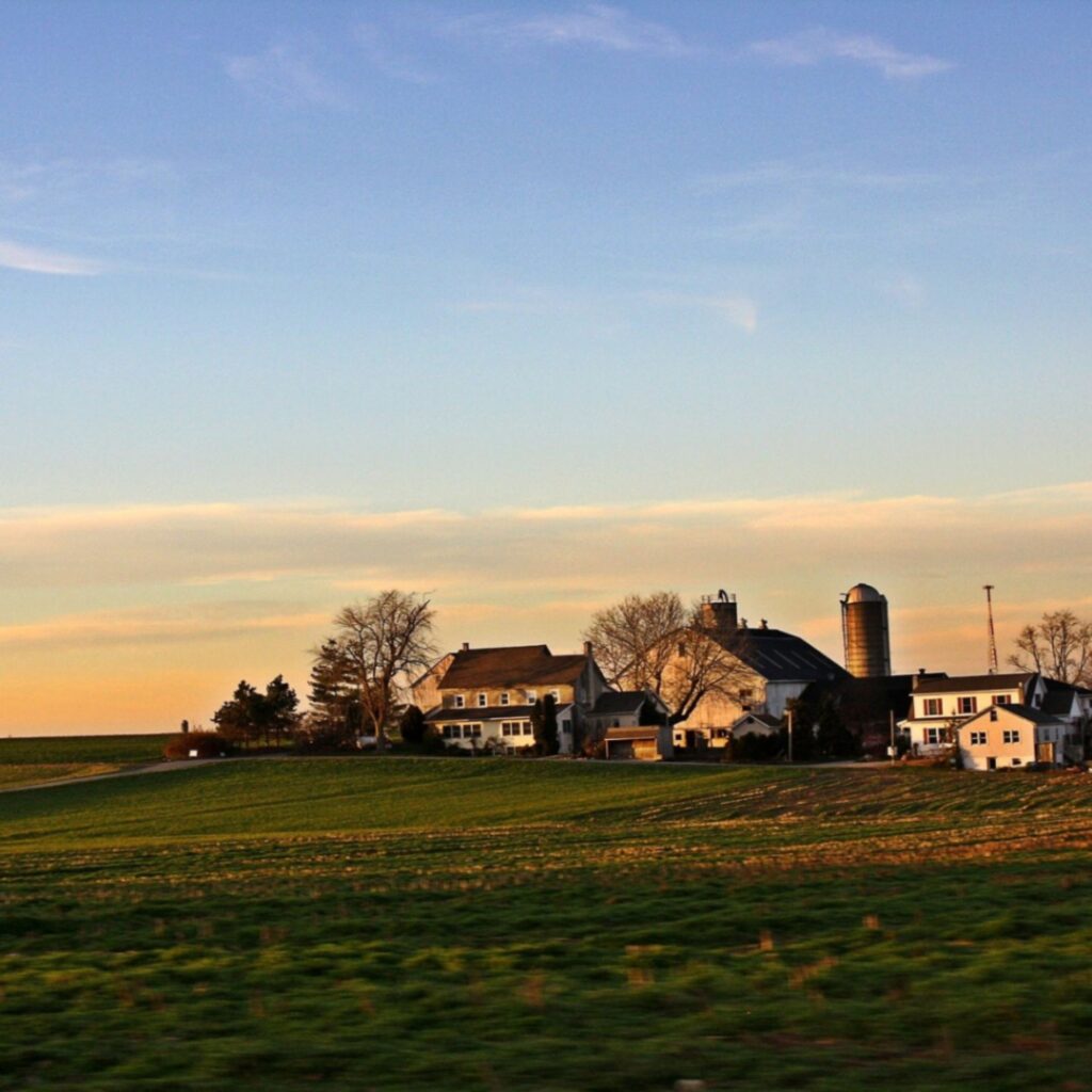 A family farm surrounded by open fields at sunset, representing the rural communities that depend on strong local organizations and sustainable resources to support long-term growth and well-being.