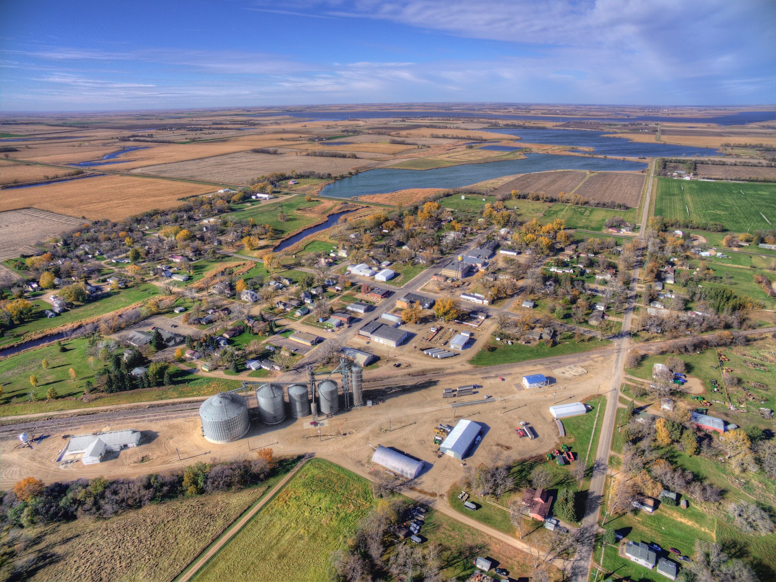 Aerial view of a small rural town surrounded by farmland, grain silos, and a lake, representing rural hospital communities