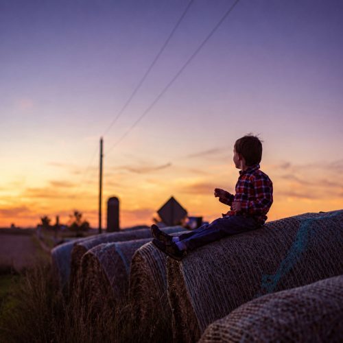 Child sitting on hay bales at sunset in rural Iowa, representing Iowa Healthy Hometowns and local rural communities.