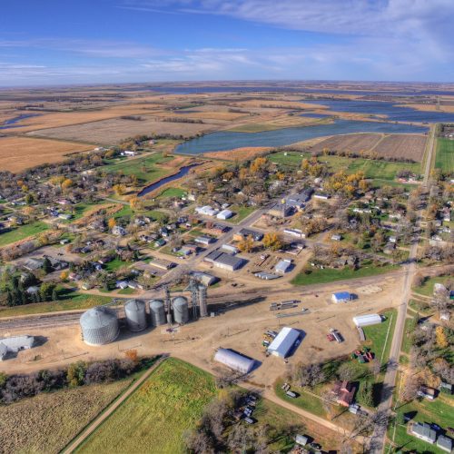 Aerial view of a small rural town surrounded by farmland, grain silos, and a lake, representing rural hospital communities