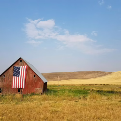 Red barn displaying an American flag beside rolling farmland and open fields.